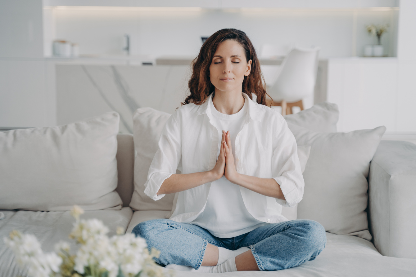 Female practicing yoga breathing exercises on couch at home. Reducing stress, wellness, meditation